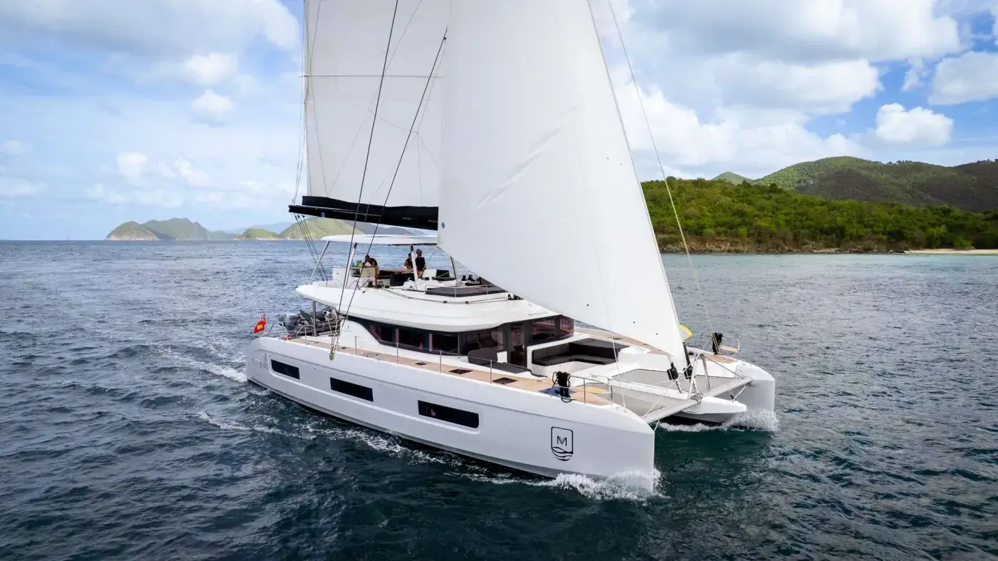 Crewed sailing catamaran under sail past green hills