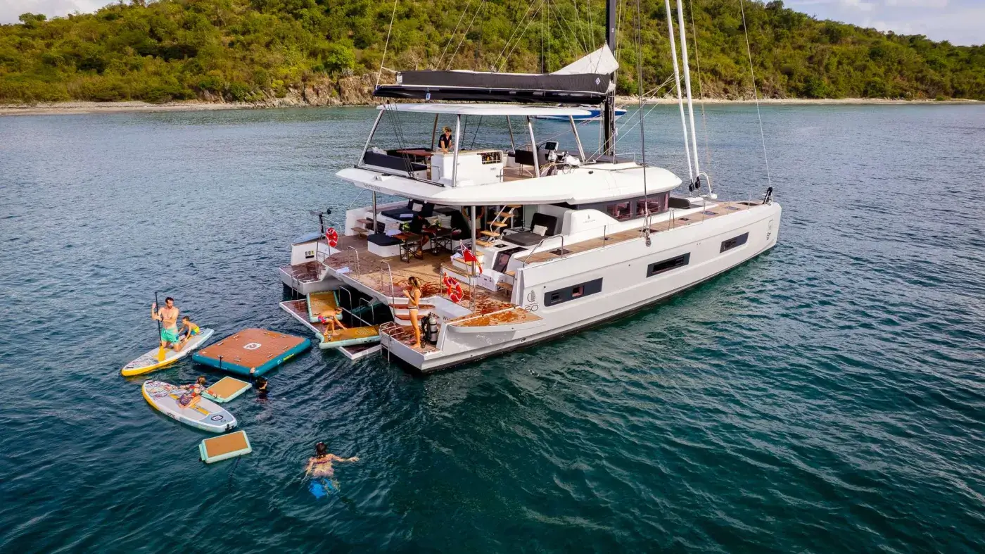 Guests swimming and paddleboarding beside a crewed catamaran at anchor